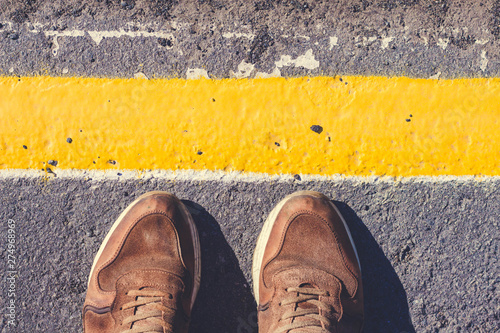 A person is standing next to the yellow line drawn. Shoes stoin on the pavement gray shade.