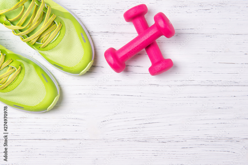 Fitness concept, green sneakers and pink dumbbells on wooden background, top view with copy space Fitness concept, green sneakers and pink dumbbells on wooden background, top view with copy space