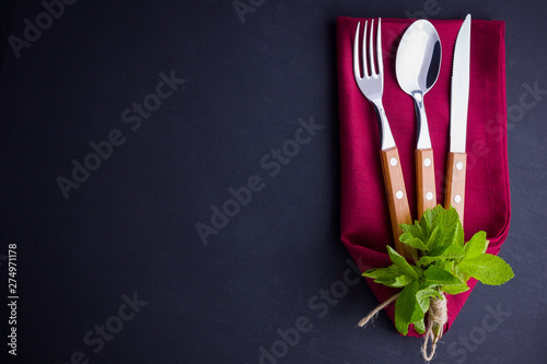 Cutlery set. Knife, spoon, fork on slate stone. Сutlery with burgundy napkin and twine. Mint on black background. Table setting. Top view