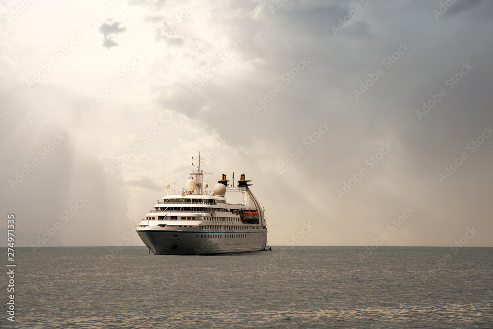 A luxury cruise ship anchored offshore with sun rays filtering through clouds, Portofino, Genoa, Liguria, Italy