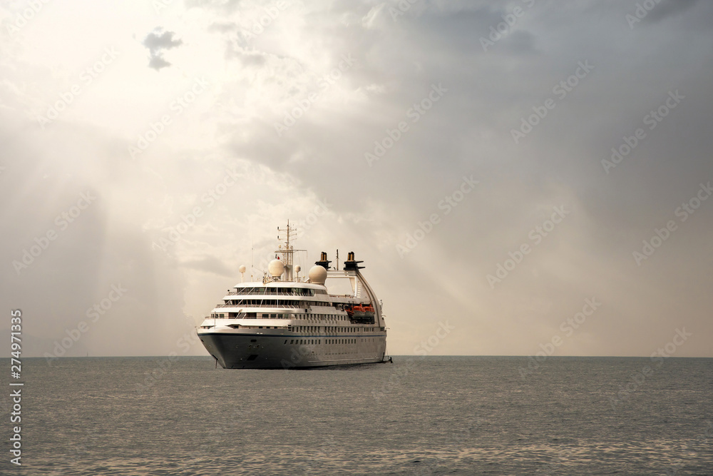 A luxury cruise ship anchored offshore with sun rays filtering through clouds, Portofino, Genoa, Liguria, Italy A luxury cruise ship anchored offshore with sun rays filtering through clouds, Portofino, Genoa, Liguria, Italy