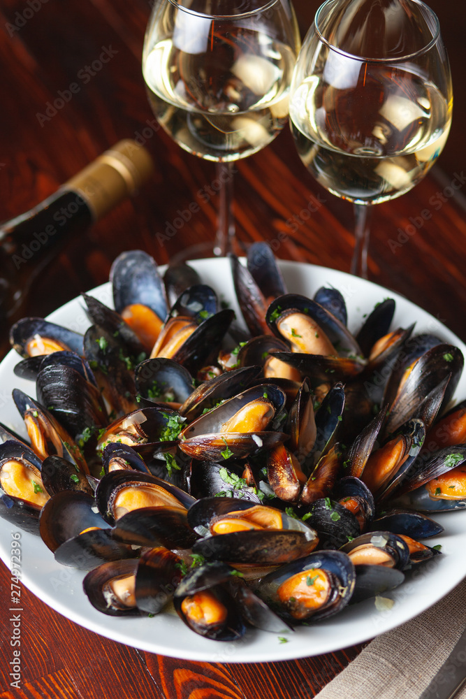 Fine dining in a seafood restaurant: a big dish of mussels with bottle of white wine with two wine glasses, on dark background Fine dining in a seafood restaurant: a big dish of mussels with bottle of white wine with two wine glasses, on dark background