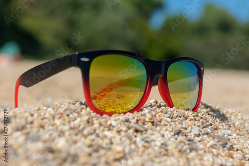 Mirrored sunglasses close up on the beach sand