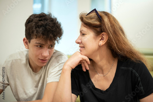 A middle-aged woman is good spending time with her son in a cafe, they sit and talk. Mom looks at her teenage son with love. Focus on mother