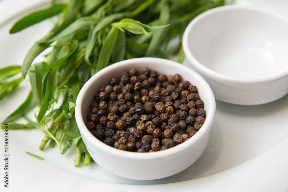 Black pepper in white bowl over white background . Saucer dish with black pepper peas isolated on white background . Dry black peppers isolated with path . Black pepper in white bowl over white background . Saucer dish with black pepper peas isolated on white background . Dry black peppers isolated with path .