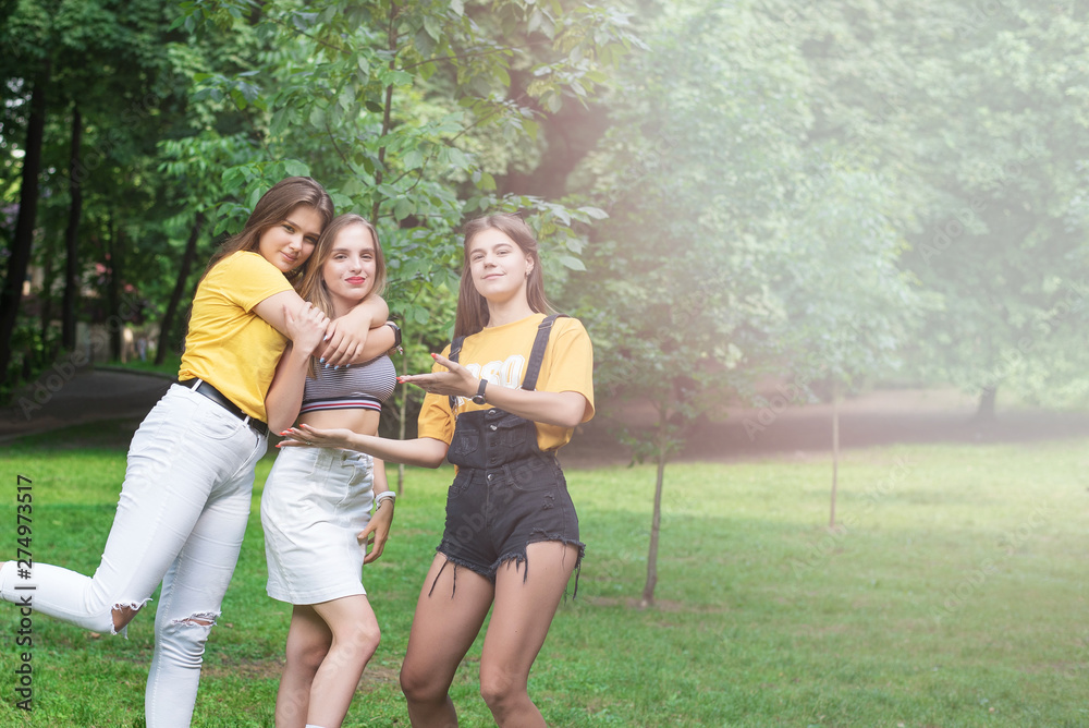 Obraz premium Three nice teen girls having fun in the park. Excellent sunny weather. Summer concept. Hugging. Lifestyle. Trendy Hipster Girls