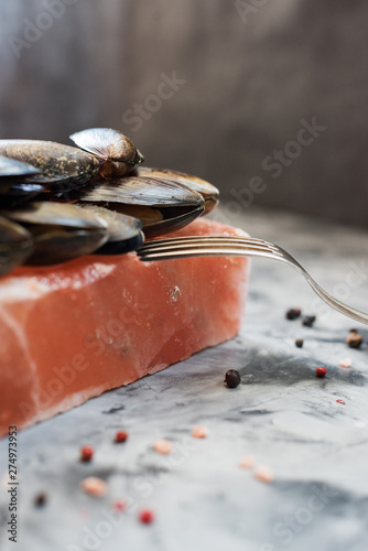 Salt block cooking. Raw mussels in shells roasted on pink Himalayan salt on concrete background side view