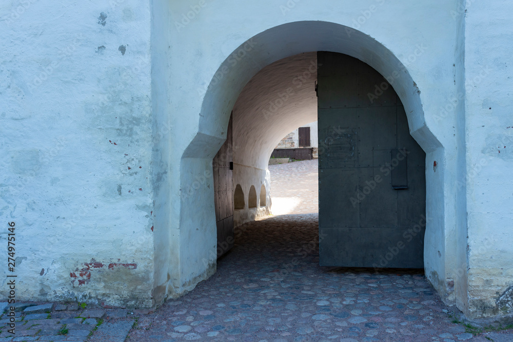 A door and an arch in a thick stone fortress wall leads to the inner paved courtyard of the medieval historic Abo castle in the city of Turku in Finland on a sunny summer day.