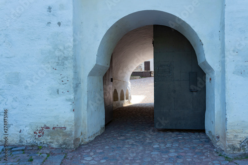 A door and an arch in a thick stone fortress wall leads to the inner paved courtyard of the medieval historic Abo castle in the city of Turku in Finland on a sunny summer day. © NATALIA