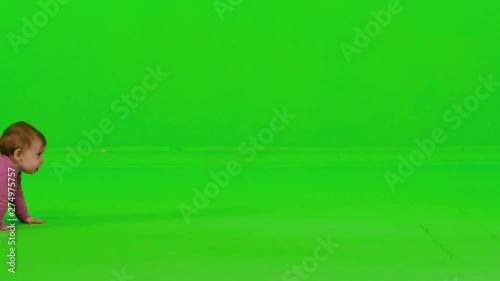 Cute baby girl crawling from side to side, stops in the middle, looks to the camera, laughs and continues, over a green screen.