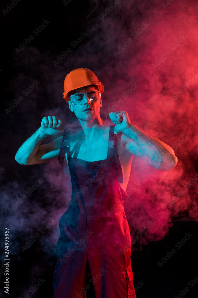 sexy shirtless fireman in overall and hardhat in smoke on black