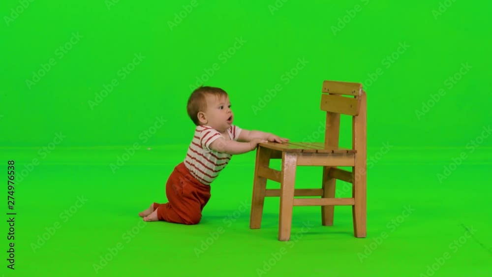 Laughing happily while standing using a chair by a cute baby girl over a green screen. Laughing happily while standing using a chair by a cute baby girl over a green screen.