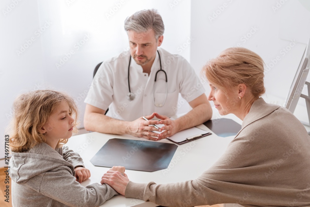 Mom and cute sick son in front of the handsome pediatrician's desk Mom and cute sick son in front of the handsome pediatrician's desk