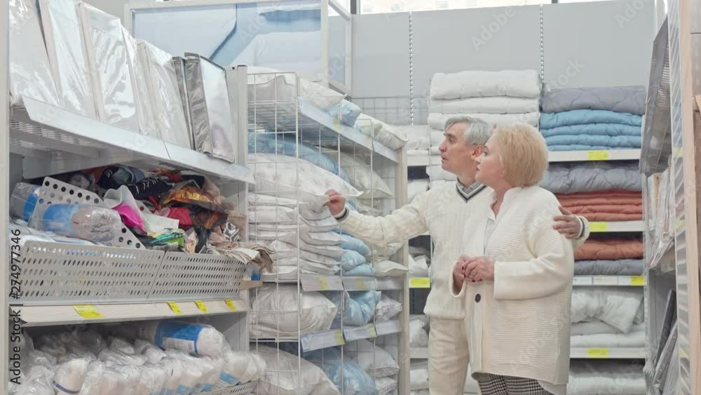 Happy retired senior couple walking in furnishings store, shopping for home goods. Elderly woman and her husband choosing textile for home. Retirement, pensioner discount concept Happy retired senior couple walking in furnishings store, shopping for home goods. Elderly woman and her husband choosing textile for home. Retirement, pensioner discount concept