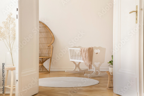 White open double door in elegant apartment with nursery designed with white crib and wicker peacock chair, real photo with copy space photo