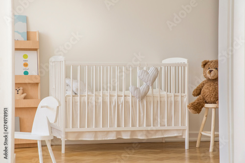 Teddy bear, rocking horse and white wooden crib with heart shaped pillows in scandinavian design interior, real photo with copy space