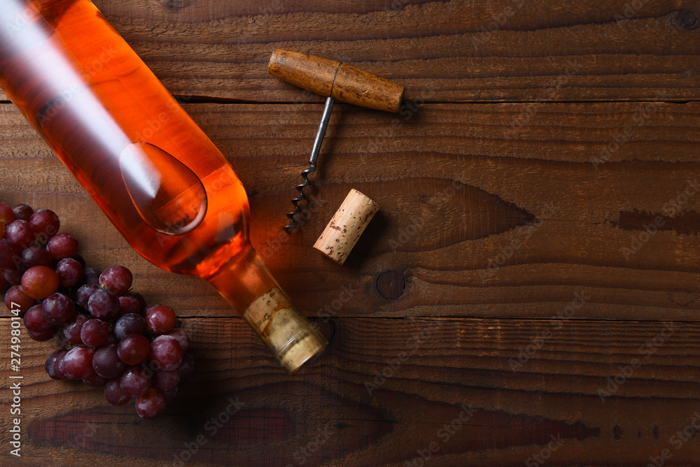 A blush wine bottle on a dark wood table with grapes and corkscrew, and copy space.