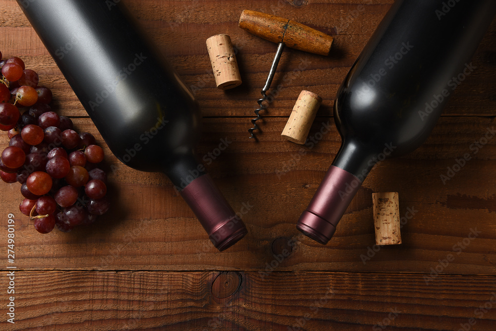 Two Cabernet Sauvignon wine bottle short from directly above on a dark wood table with grapes corks and cork screw and copy space.