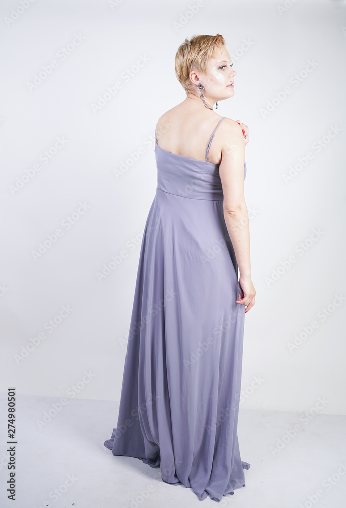 elegant thick female in a grey long dress. pretty plus size woman in evening dress standing on white studio background. short hair chubby girl in gray clothes posing alone.
