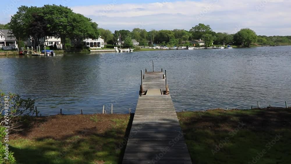 Locked off shot view of private jetty stretching out into river with houses on the other bank Locked off shot view of private jetty stretching out into river with houses on the other bank