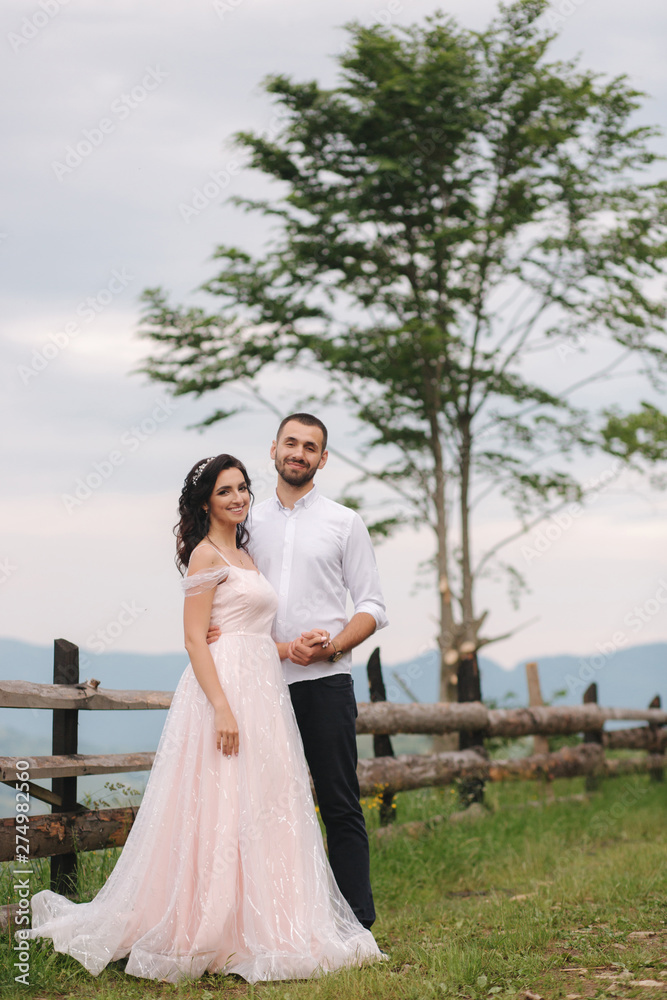 Lovestory of beautiful couple in the mountains, Handsome bearded man with beautiful and charming woman. Couple stand in front of beautiful tree