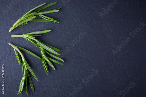 Rosemary branches on black background. Fresh rosemary on slate stone. Herbs for cooking meat dishes with copy space. Top view