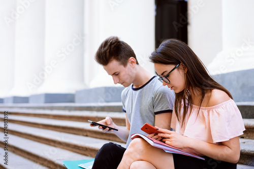 Students while break sitting on stairs of the university using mobile phones and paying no attention to one another