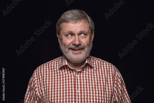 Close up portrait of senior man isolated on black studio background. Photoshot of real emotions of male model. Dreaming and smiling, hopeful and happy. Facial expression, human emotions concept.