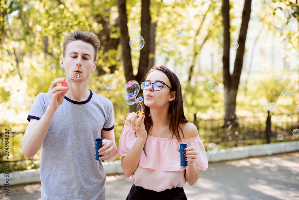 Obraz premium Two friends having fun together blowing soap bubbles in the park