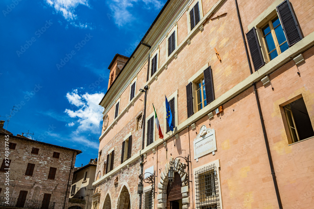 The municipal building of Spello with the Italian and European flag (EEC). The tower with the clock. Perugia, Umbria, Italy.