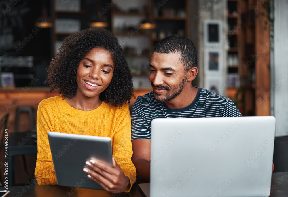 © StratfordProductions - Young couple with laptop and digital tablet in café