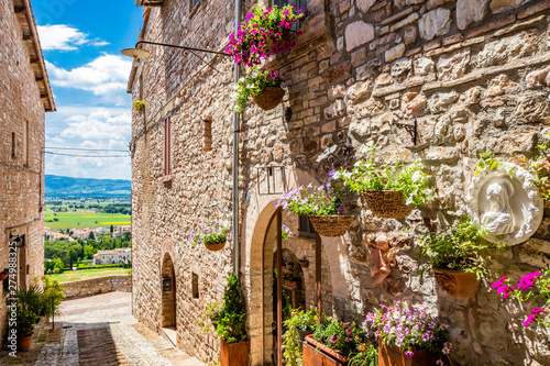 A characteristic alley of the medieval village, with stone and brick houses, plants and flowers on the windows. In Spello, province of Perugia, Umbria, Italy. photo