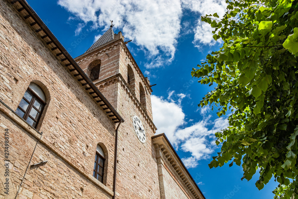 Fototapeta premium The church of Santa Maria Maggiore, the portal adorned with Romanesque friezes and the Romanesque bell tower with the clock. In Spello, province of Perugia, Umbria, Italy.