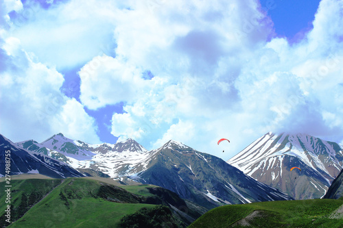 Mountain panorama with paragliders. Scenic blue sky and mountain peaks in snow.