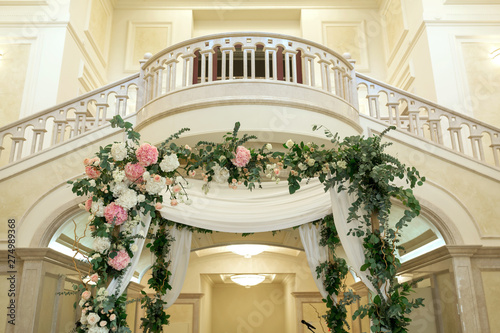Beautiful wedding huppah decorated with fresh fresh flowers from hydrangea and eucalyptus sheets in a large beautiful wedding hall with a balcony. Wedding floristry © Kate