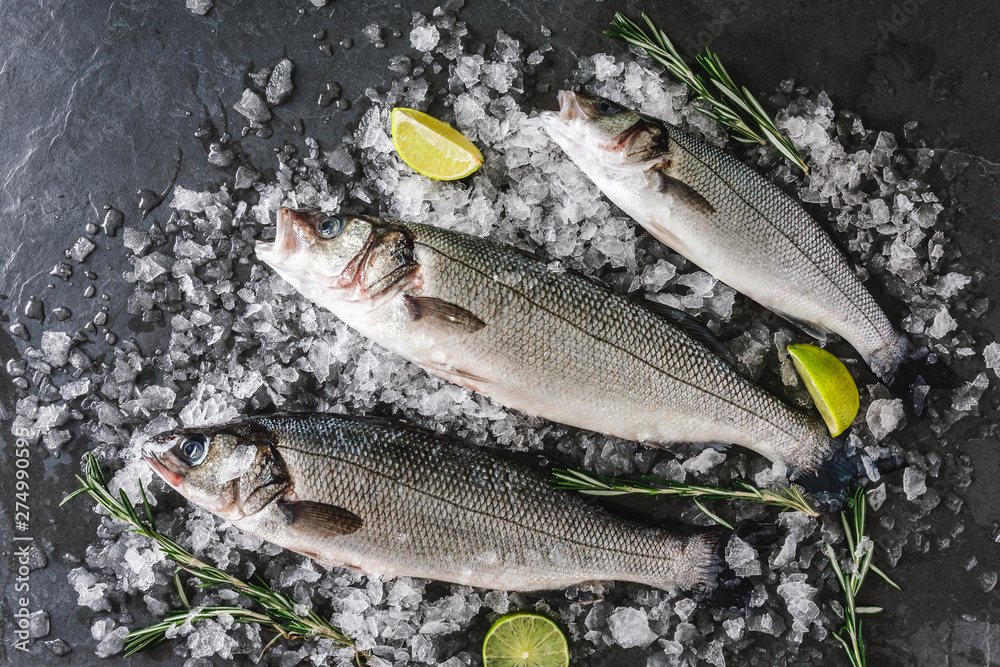 Fresh raw carp fishes with spices, lemon, rosemary on ice over dark stone background. Creative layout made of fish, top view, flat lay