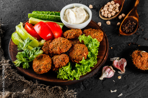 Roasted chickpeas falafel patties with garlic yogurt sauce, served with lettuce and fresh vegetables in a plate over dark stone background. Healthy vegan food, clean eating, dieting, top view photo