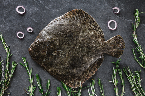 Raw whole flounder fish with rosemary, onions and spices on dark stone background. Creative layout made of fish, top view photo