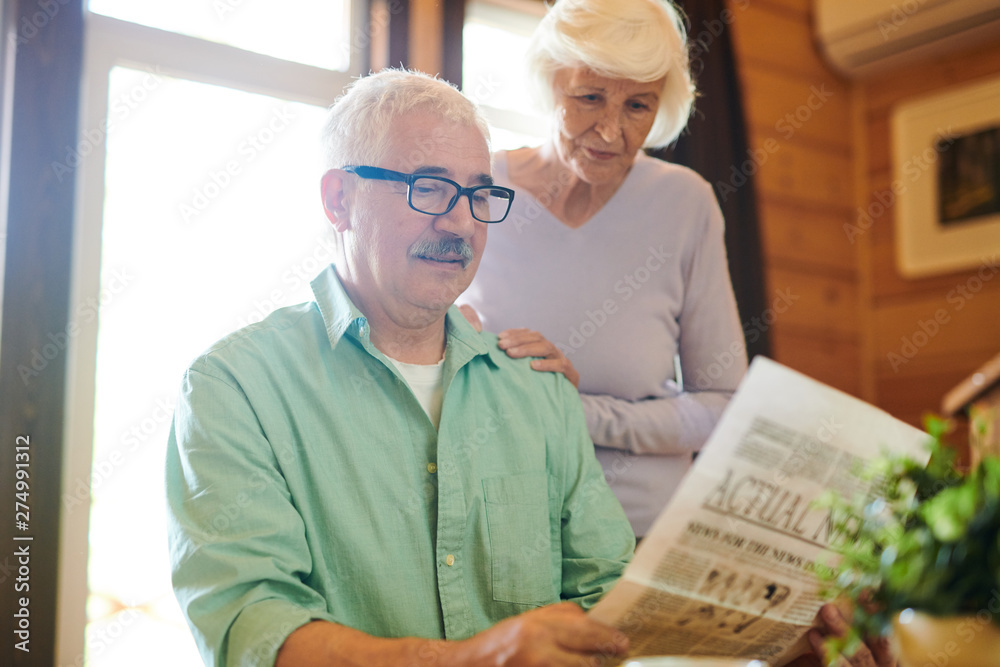 Serious matue man reading fresh news to his wife Serious matue man reading fresh news to his wife