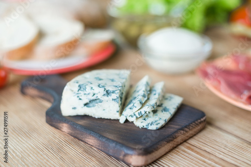 Fototapeta Naklejka Na Ścianę i Meble -  Sliced blue cheese on a wooden background and different products. Preparation for cooking snacks.