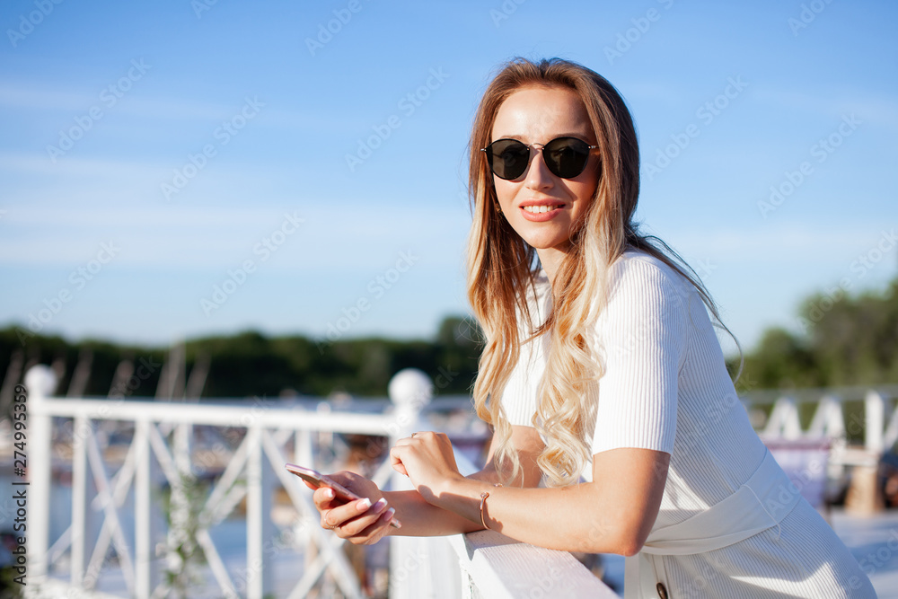 Elegant charming woman texting romantic message on mobile phone. Portrait of luxary lady in glasses enjoying summer sunset in cafe outdoor. Communicating by smartphone in travel..