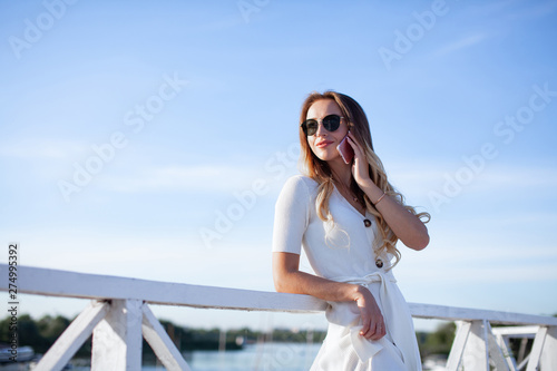 Elegant charming woman talking on the mobile phone. Portrait of luxary lady in glasses enjoying summer sunset in cafe outdoor. Communicating by smartphone in travel. .