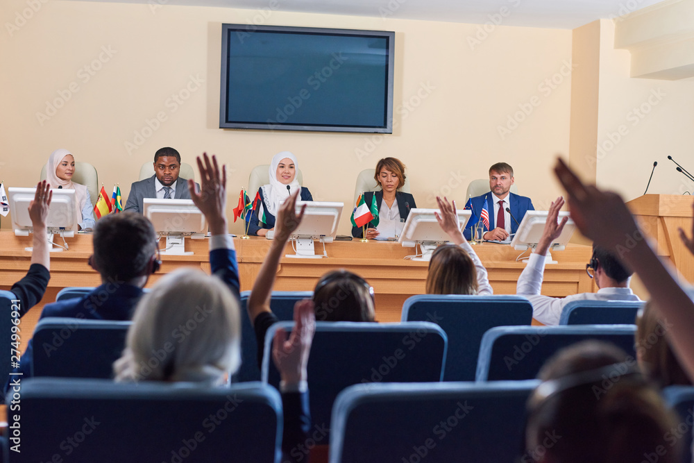 Audience in armchairs raising their hands to ask questions