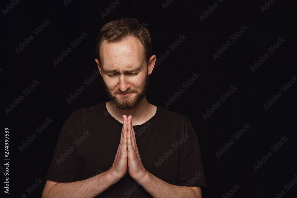 Close up portrait of young man isolated on black studio background. Photoshot of real emotions of male model. Praying with closed eyes and crying. Facial expression, human emotions concept. Close up portrait of young man isolated on black studio background. Photoshot of real emotions of male model. Praying with closed eyes and crying. Facial expression, human emotions concept.