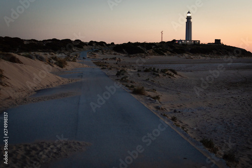 Road covered with sand from the dunes, road towards lighthouse of Trafalgar, Cadiz, Spain at sunset