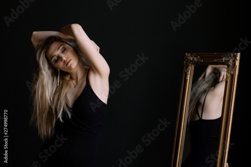 Beautiful slim young woman posing on a black background near the mirror photo