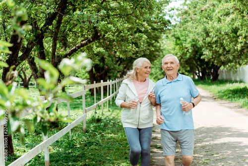selective focus of cheerful retired man running near senior wife in park