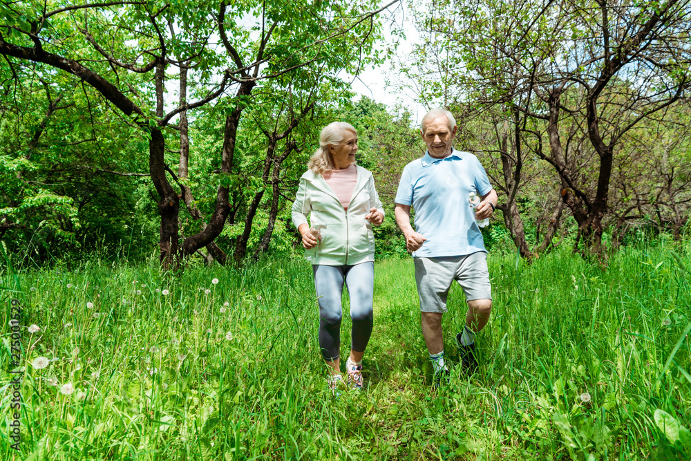 happy woman with grey hair looking at husband while running in park