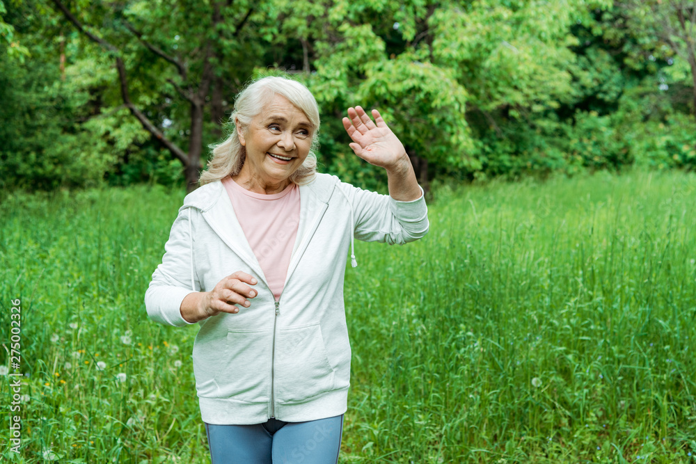cheerful senior woman with grey hair waving hand in park cheerful senior woman with grey hair waving hand in park