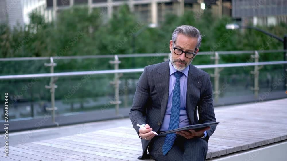  Mature male entrepreneur working with startup project pondering on idea and feeling good when getting great result, successful man in formal suit writing text on touch pad via stylus pen